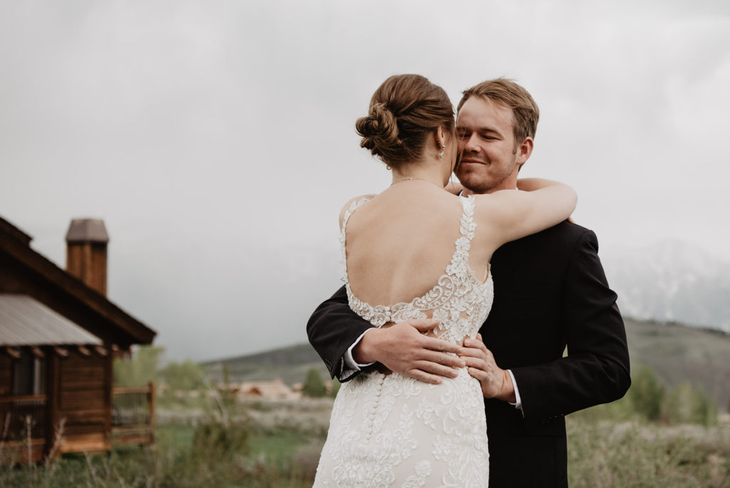 groom hugging his bride around the waist as he smiles after their wedding first look in the Tetons with Jackson Hole wedding photographers 