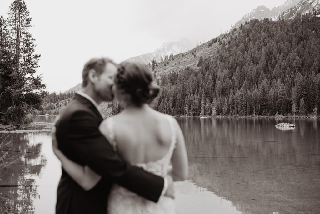 black and white wedding picture of bride and groom hugging and kissing on a lake