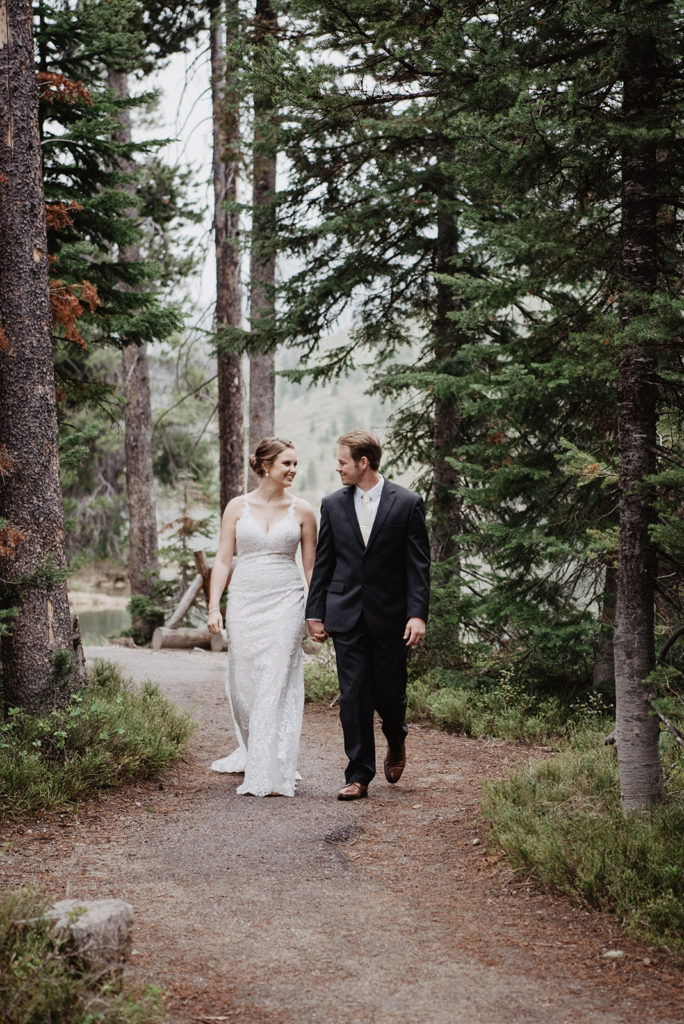 bride and groom holding hands while walking through the woods together for their Jackson Hole wedding