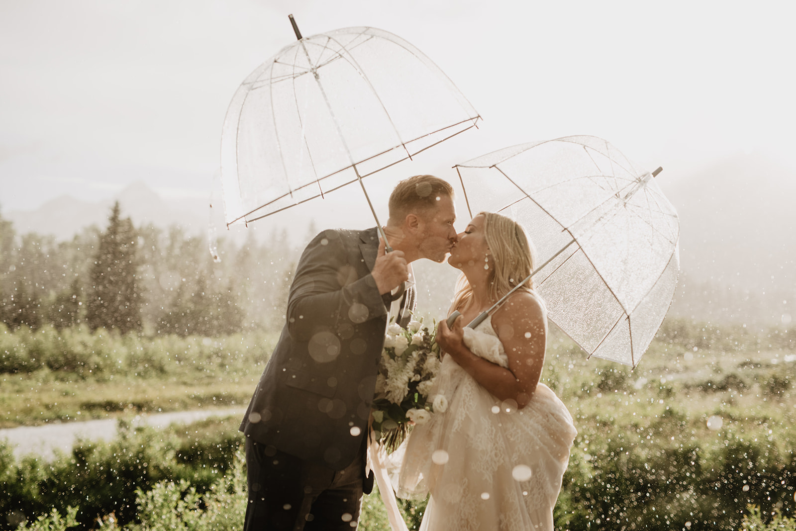 bride and groom kissing as the rain comes down on them and the sun shines through the clouds taken by Jackson Hole photographer
