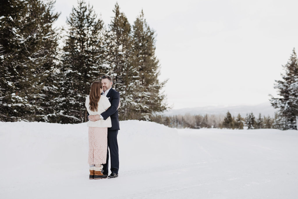 bride and groom embracing each other in a snow filled field in the Tetons for their winter wedding pictures with Jackson Hole wedding photographer with pine trees in the distance 