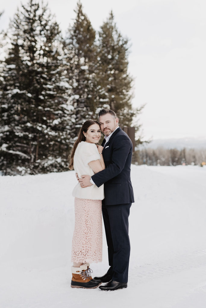 bride and groom hugging each other for their outdoor winter wedding pictures with Jackson Hole wedding photographer with tall pine trees in the distance covered in snow