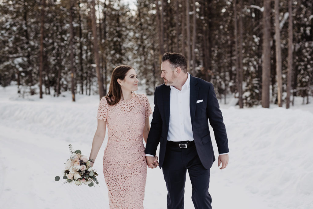 bride and groom holding hands and walking through the woods together for their outdoor winter wedding with Jackson Hole wedding photographer 