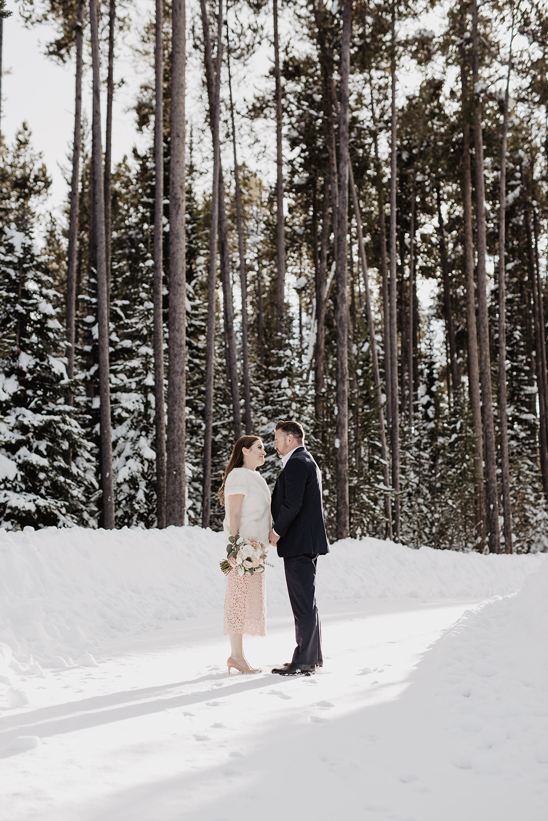 Jackson Hole wedding photographer captured bride and groom leaning into each other romantically in a pine wood forest for their winter wedding