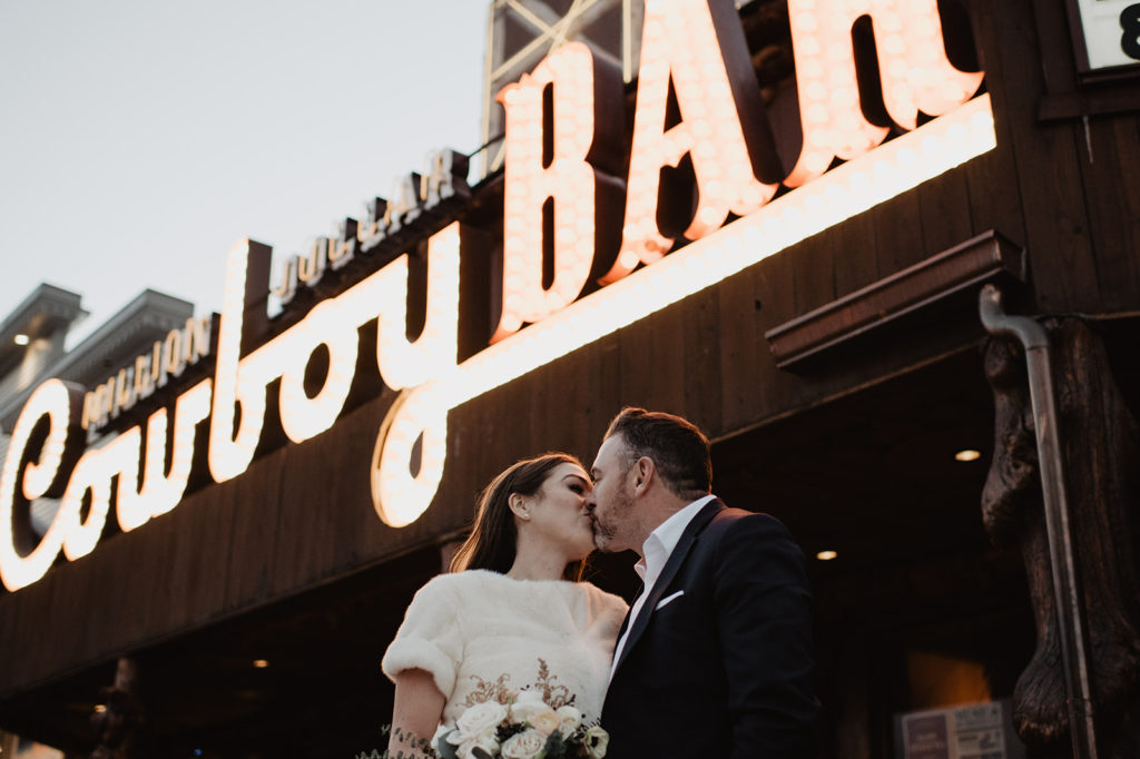 bride and groom kissing under the Cowboy Bar sign for their winter wedding in the Tetons with Jackson Hole wedding photographer