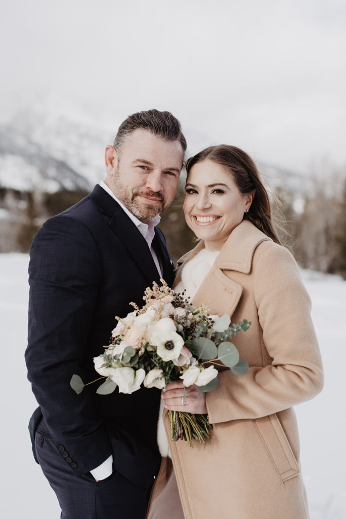 bride and groom standing together in their coats for there outdoor winter ceremony while holding each other with brides floral bouquet