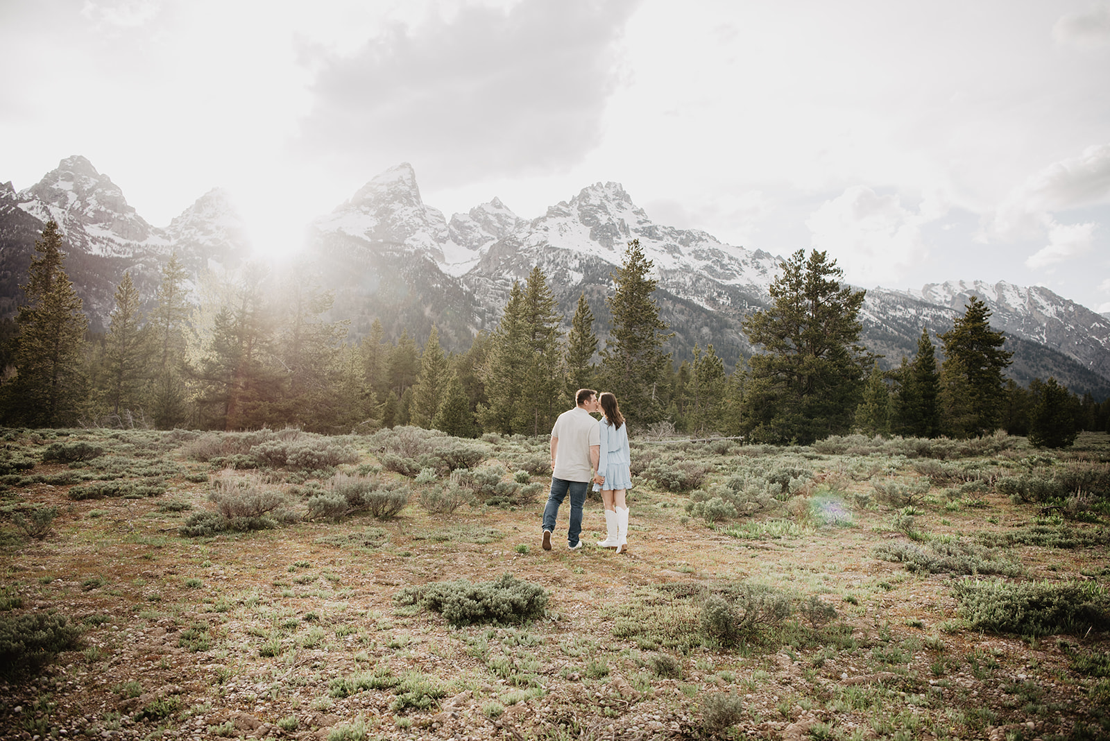 Jackson Hole Wedding photographers captured bride and groom at sun set walking and kissing in a sage brush field