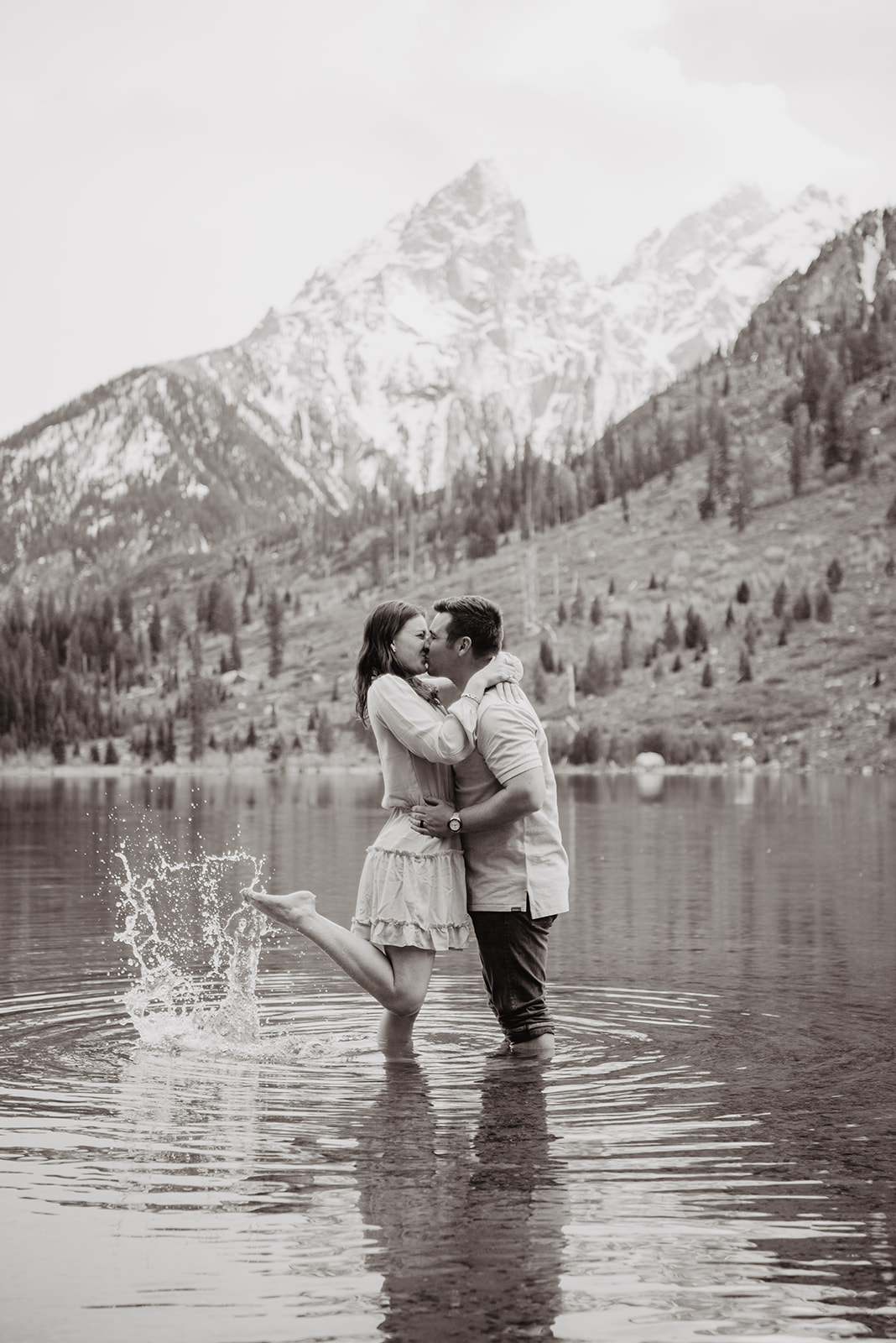 black and white wedding pictures in the Tetons with Jackson Hole Wedding photographers with bride and groom hugging and kissing while playing in the water together with the mountains behind them