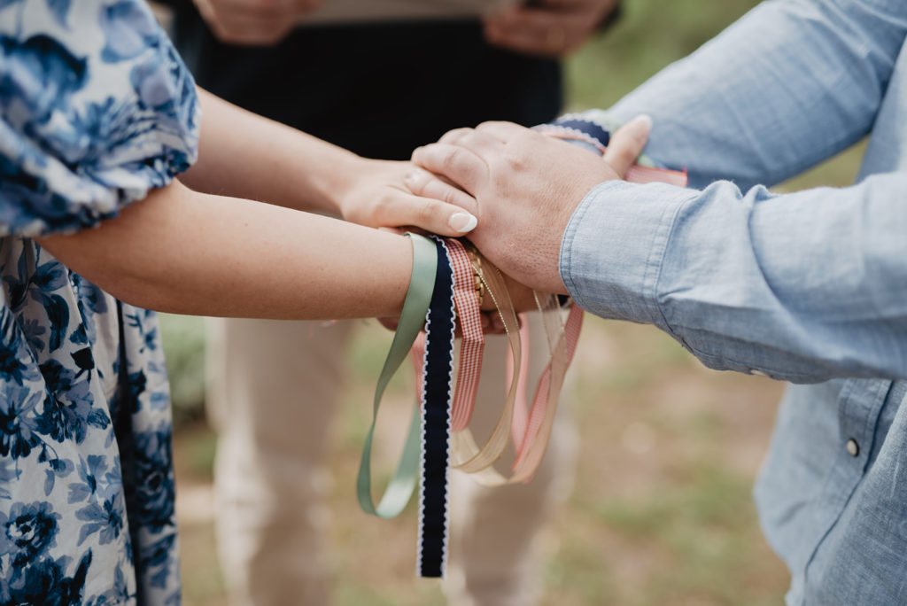 outdoor ceremony with bride and groom holding hands as well as the knot they tied together for their wedding ceremony tradition captured by jackson hole wedding photographers 