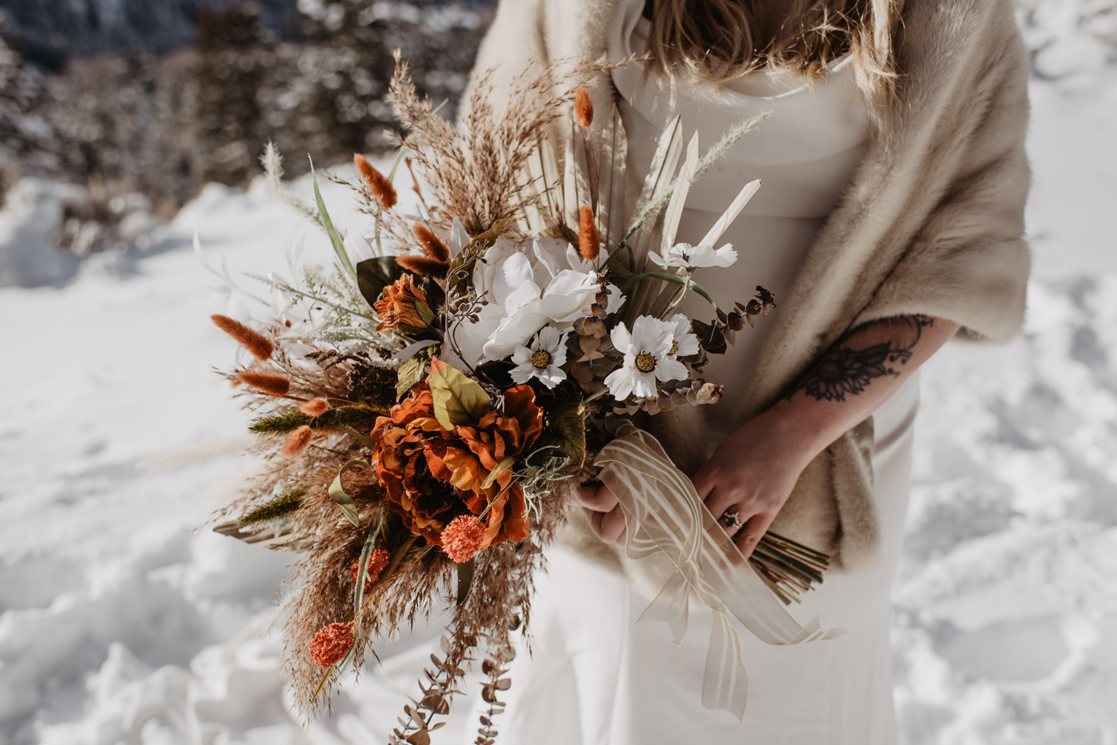 winter wedding in Jackson Hole wedding bouquet with orange and red hues in the florals as well as boho greenery captured by Jackson Hole wedding photographers