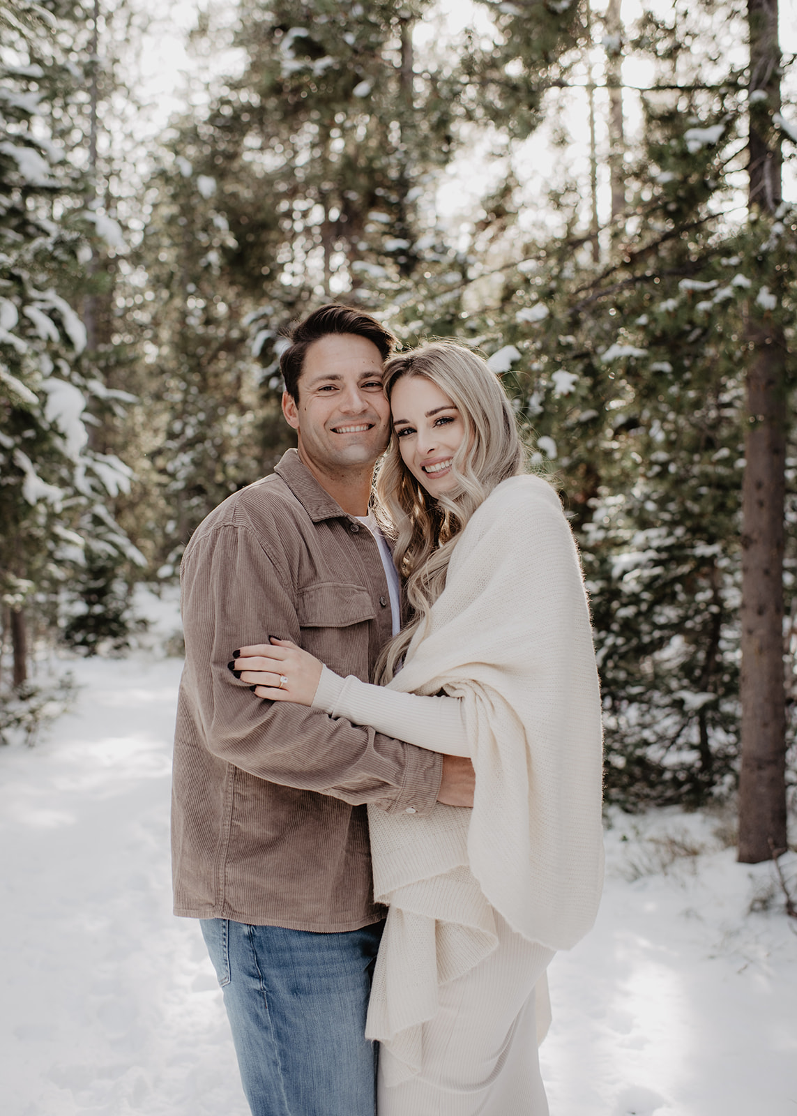 woodland engagement pictures in Jackson Hole with man and woman embracing in the forrest surrounded by snow photographed by Jackson Hole wedding photographer