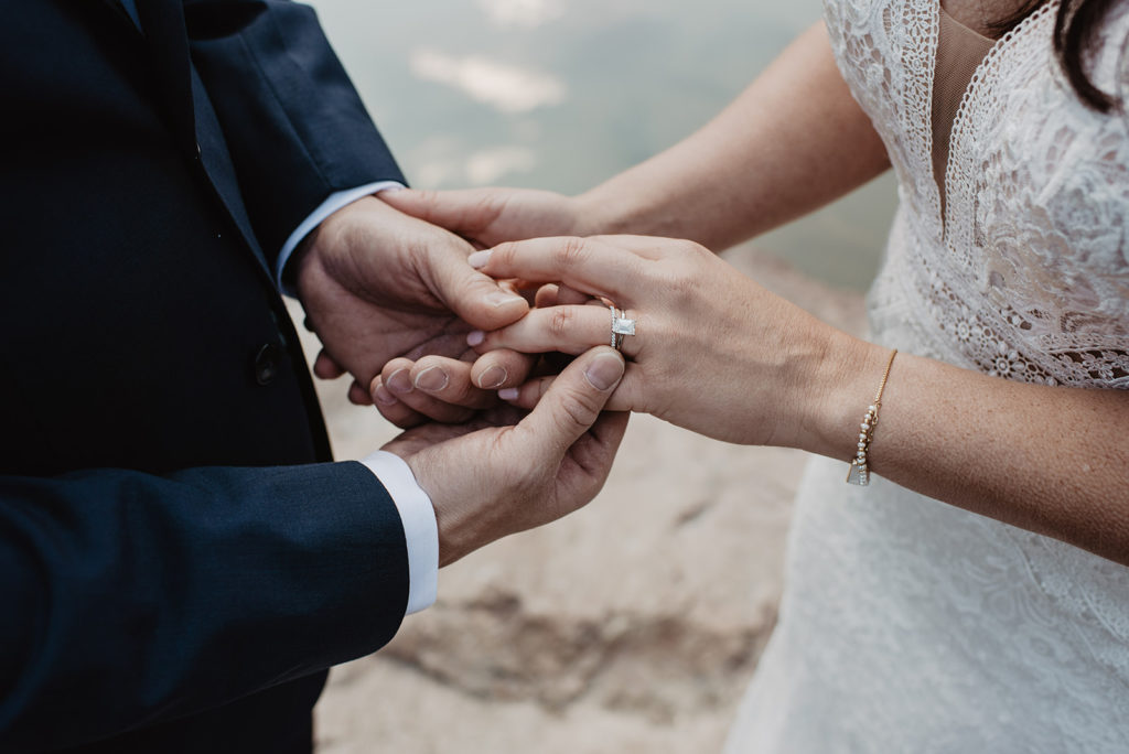 engagement rings detail shot with groom putting on his brides wedding band during their outdoor wedding band at their lake wedding captured by Jackson Hole wedding photographers