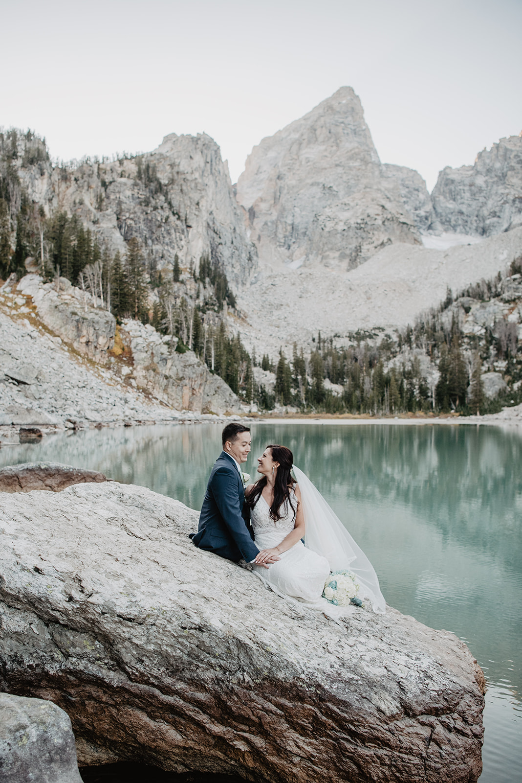 Jackson Hole wedding photographers captured wedding pictures in Grand Tetons with bride and groom sitting on a large rock at Delta Lake wedding
