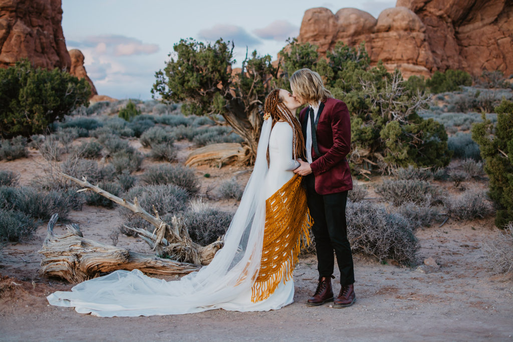 outdoor Arches National Park wedding with bride and groom kissing in the sage brush and red rock with Utah elopement photographer
