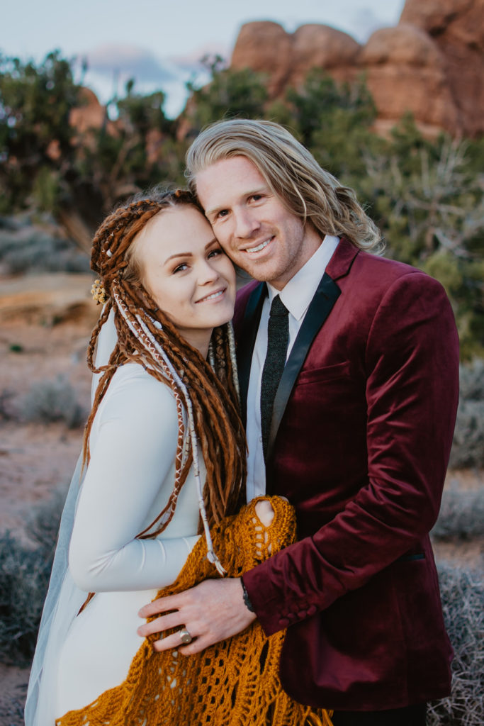 utah elopement photographer captures bridal portraits with bride and groom embracing one another after the sun sets in Moab for their Arches National Park wedding