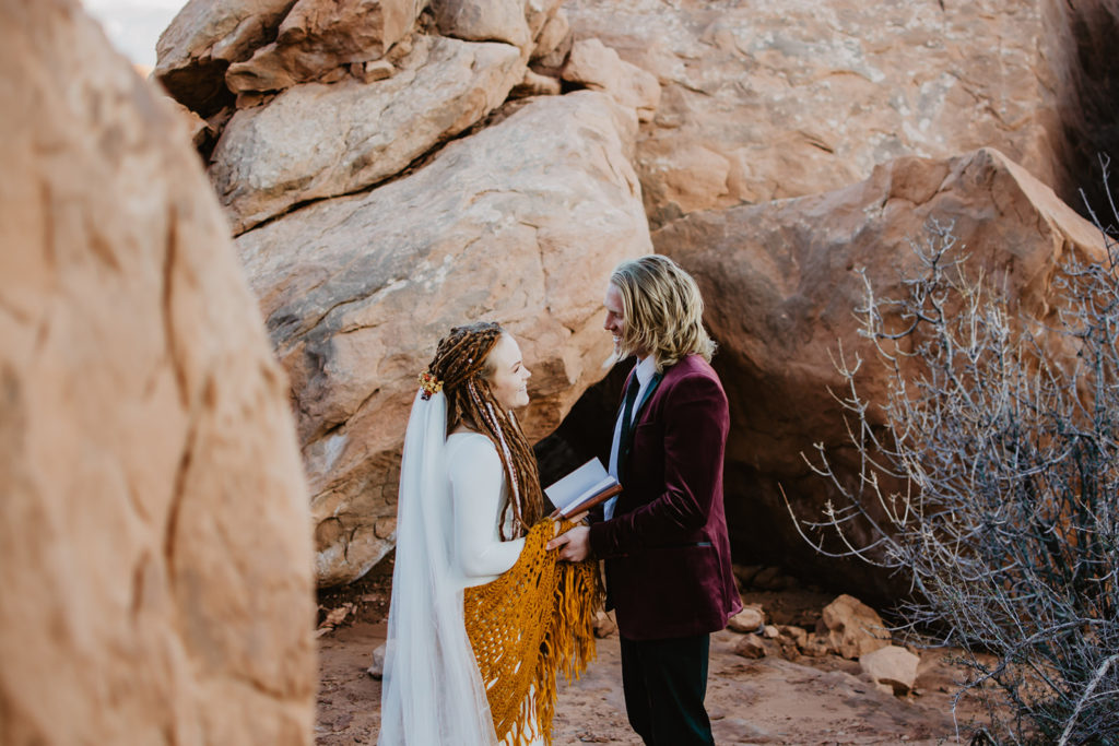 outdoor arches national park wedding ceremony with bride and groom standing among red rock and reading their vows to each other captures by utah elopement photographer