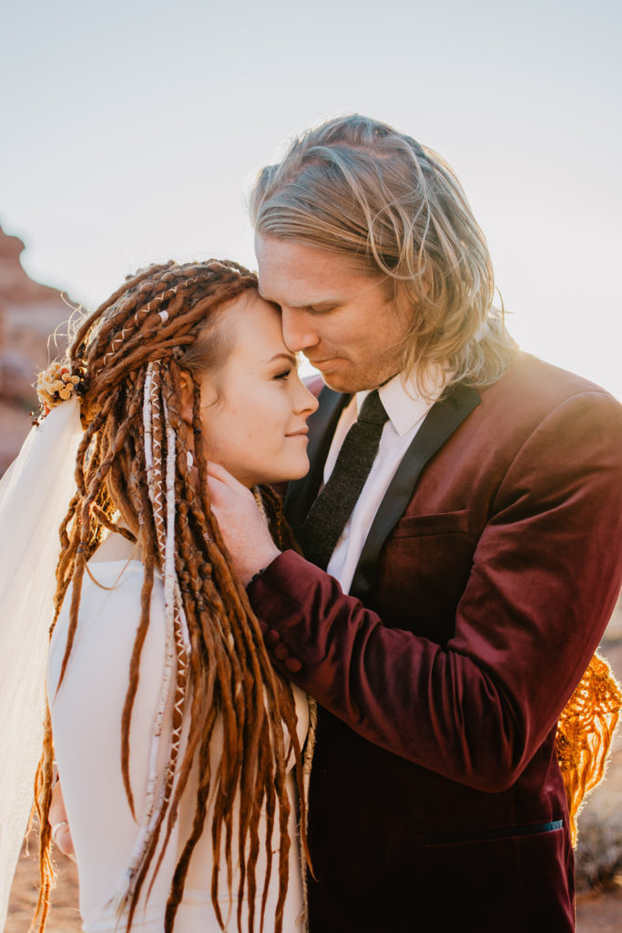 Utah elopement photographer captures romantic embrace between bride and groom as the sunsets in the distance adding a glow to their moment together for their Arches National Park wedding