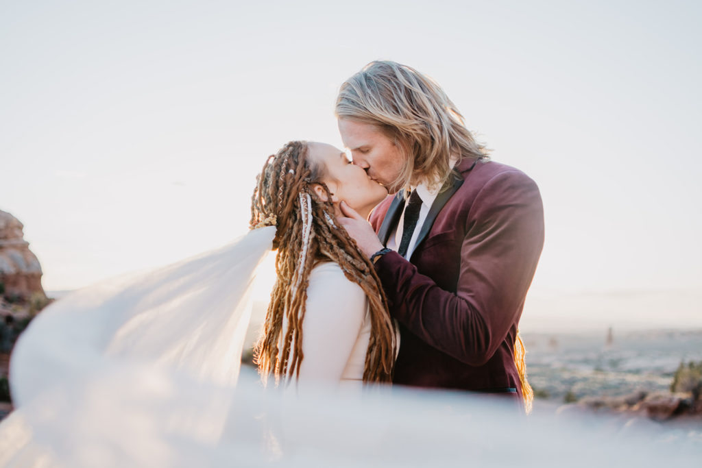 bride and groom embracing as the sunsets in the distance while the groom holding his brides face and kisses her passionately photographed by Utah elopement 