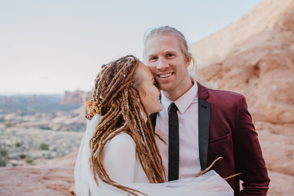 Utah elopement photographer captures bride holding her groom and leaning into him as he smiles wide at Arches National Park wedding