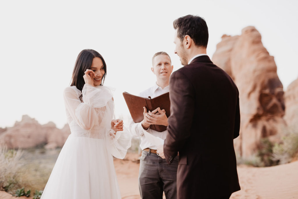 arches national park wedding photographer captures bride tearing up at her outdoor ceremony as her groom shares his vows