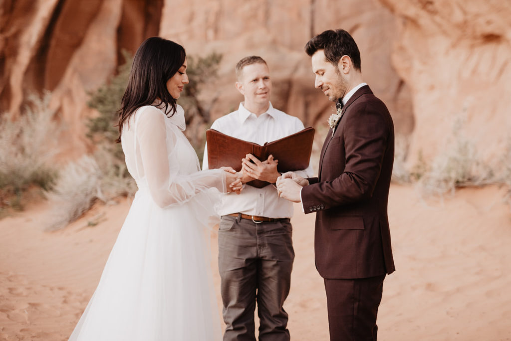 first look alternatives for destination wedding with bride and groom holding hands and praying together captured by Utah elopement photographer with red rocks as the background 