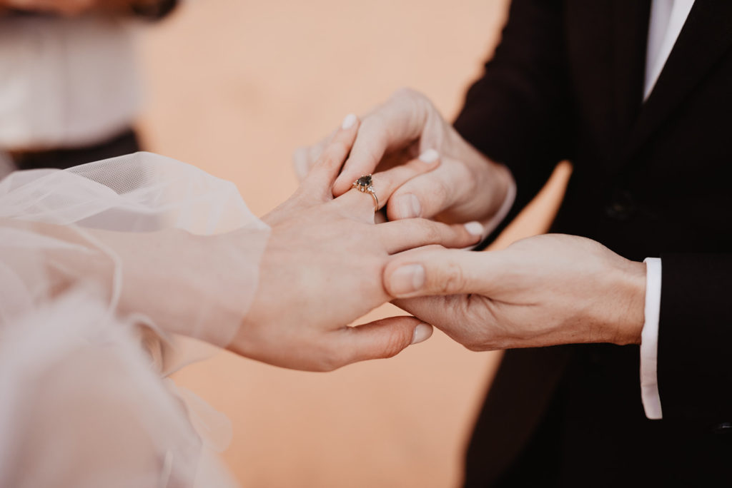 bride and groom exchange rings as the groom puts on the brides gemstone ring during their wedding ceremony in Moab with Utah elopement photographer 