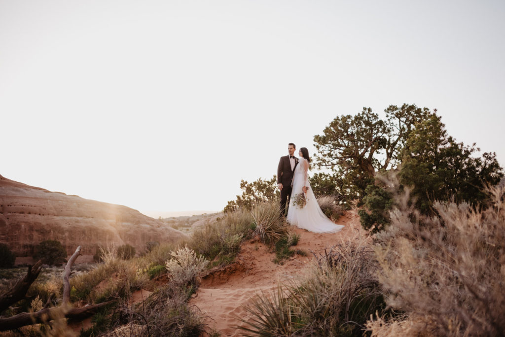 Arches National Park wedding with bride and groom on a hill with the sun setting behind the sage brush captured by Utah Elopement Photographer