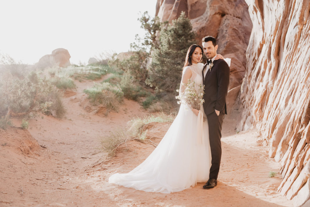 Utah Elopement Photographer photographs bride and groom embracing as the sun sets over the red rock for their Arches National Park wedding