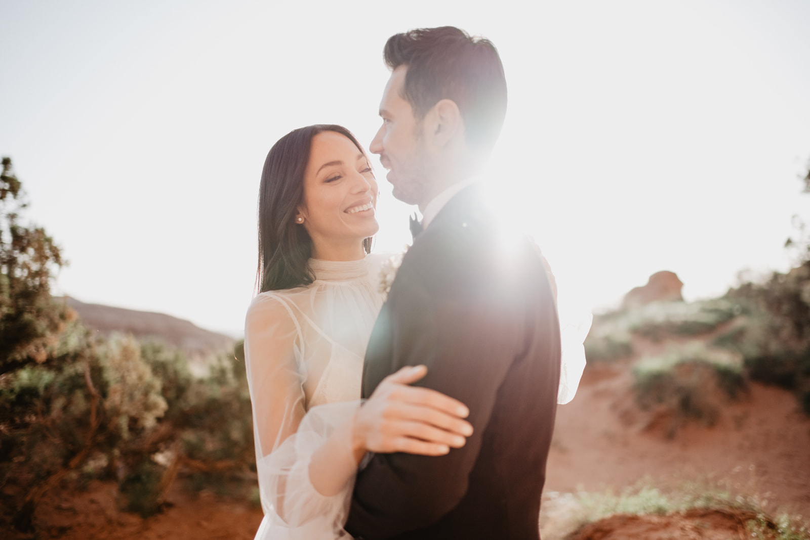 Utah Elopement Photographer photographs bride and groom embracing in the sunset surrounded by red rock and sage brush