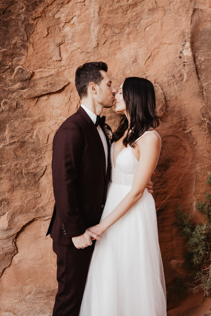 utah elopement photographer captures bride adn groom holding hands and leaning into each other and the groom kissing the bride on her nose sweetly 