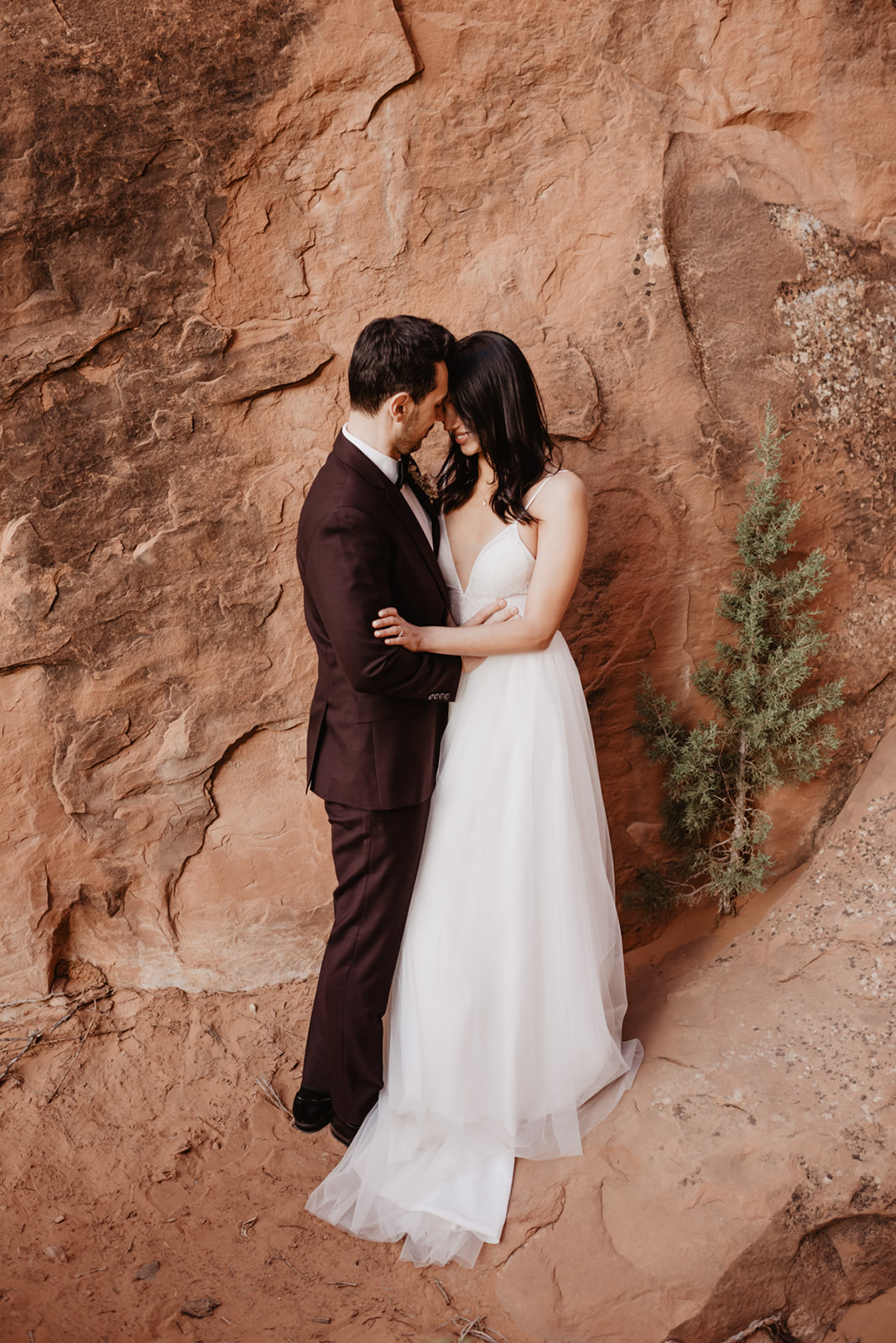 Utah Elopement photographers captures romantic wedding portraits with bride and groom embracing against red rock in Moab wedding
