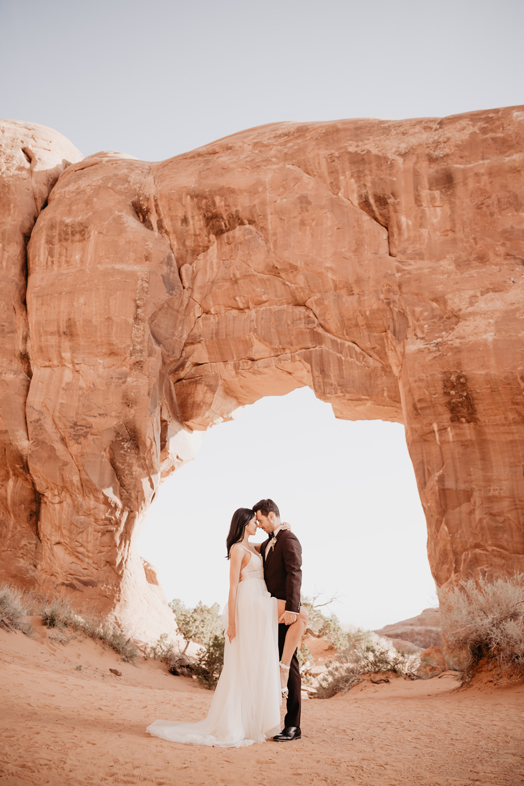 bride and groom posing under and Arch in Southern Utah for their wedding with Utah wedding photographer