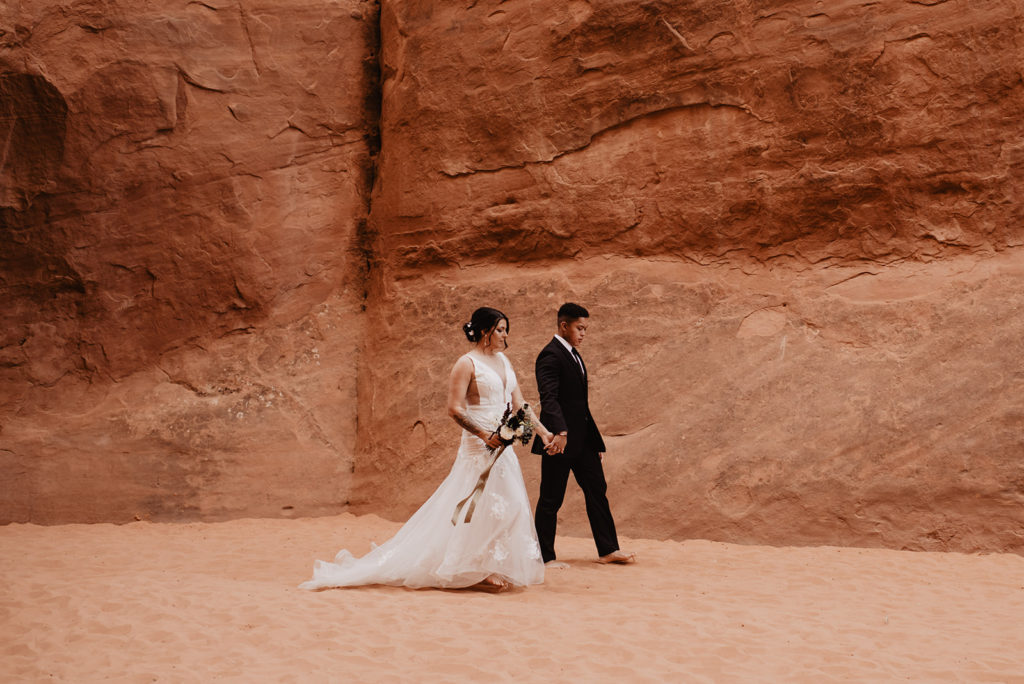 Utah Elopement Photographer captures bride and groom walking barefoot through red rock