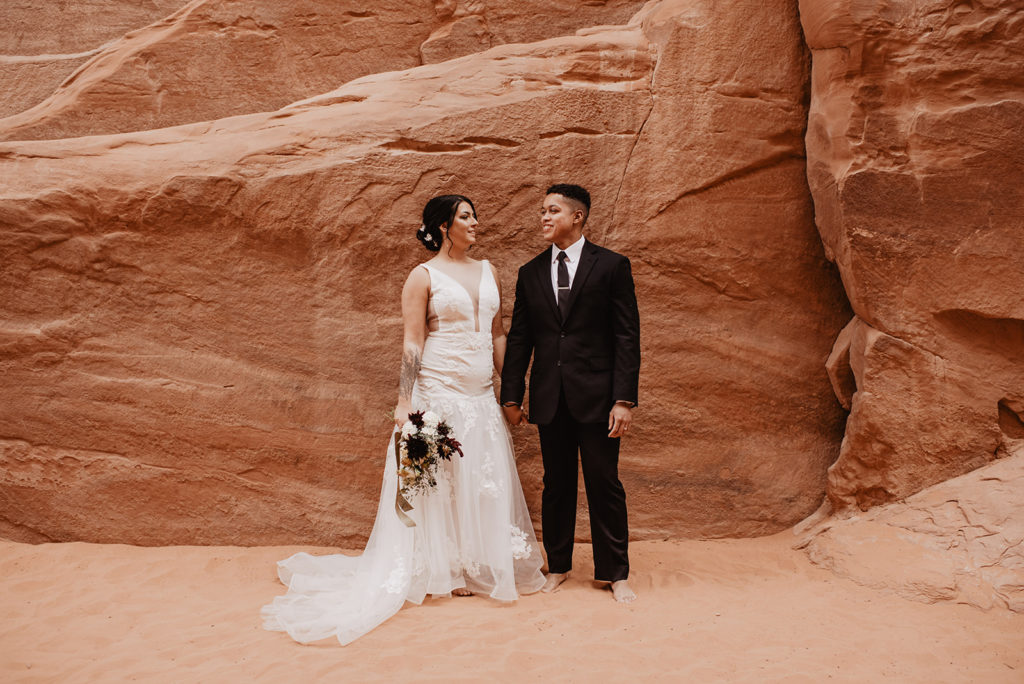 Arches National Park wedding with bride and groom holding hands and looking at one another romantically while standing against the red rocks photographed by Southern Utah elopement photographer 