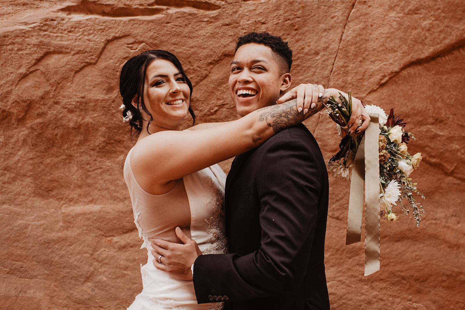 groom holding his bride around the waist while she holds her arms around his neck and they both laugh and smile for their wedding first look captured by Utah elopement photographer