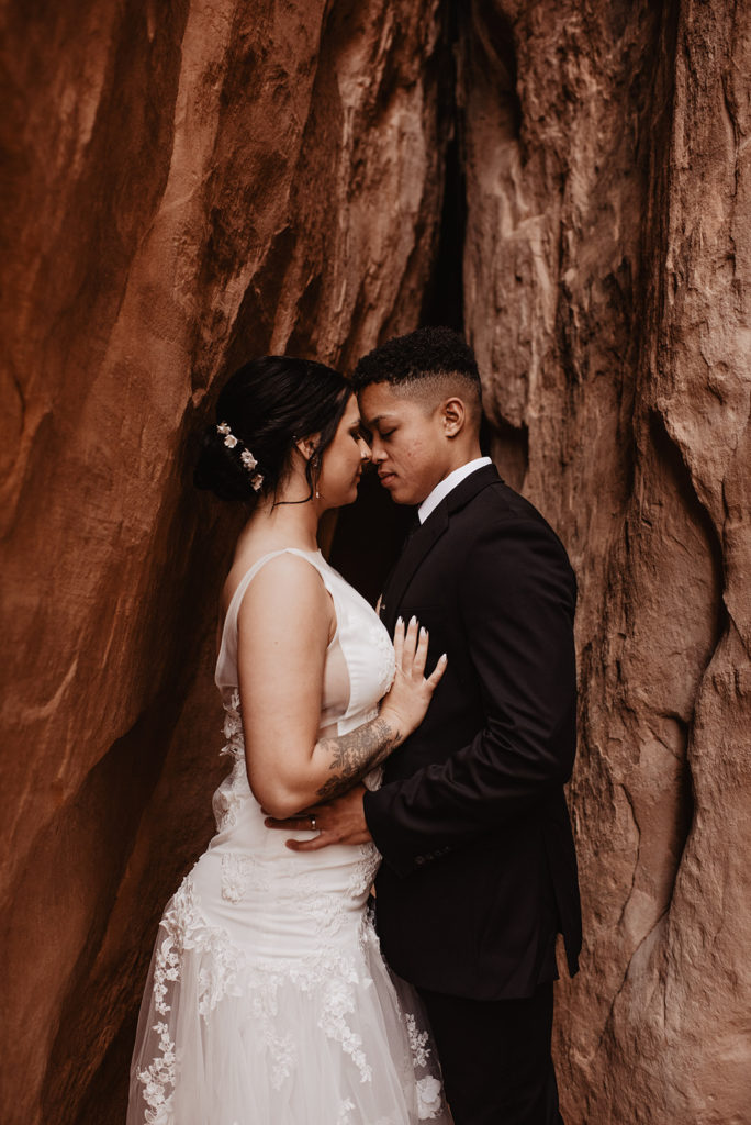 bridal portraits by utah elopement photographer with bride and groom embracing in a crevice of a large red rock mountain 