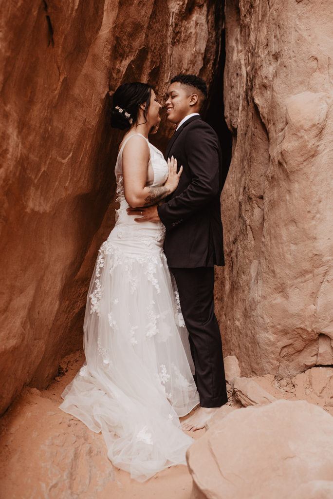 Arches National Park wedding with Utah elopement photographer capturing bride and groom embracing against red rocks in a cave 