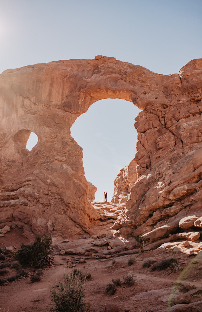 Utah Elopement Photographer captures bride and groom standing under arches. 