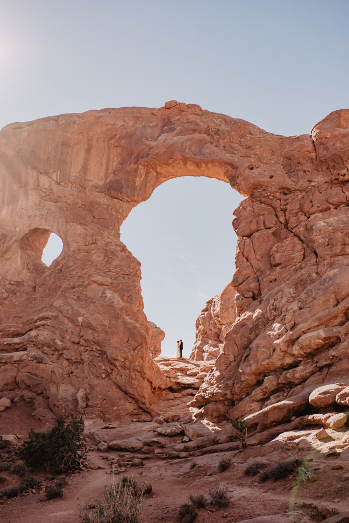 Arches National Park wedding with bride and groom embracing under a large arch in the National Park photographed by Utah elopement photographer