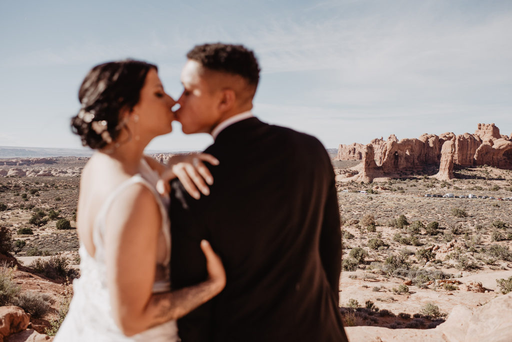 Arches National Park wedding with bride and groom hiking to the top of a mountain and kissing captured by utah elopement photographer 