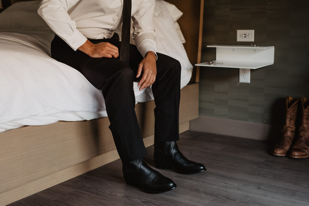 detail shot of groom sitting on the edge of his bed with his shoes on before his Utah elopement