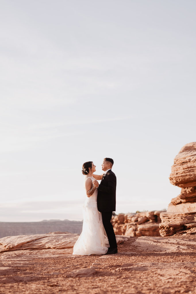 first dance for Arches National Park wedding with bride and groom holding hands and dancing together on top of a cliff captured by Utah elopement photographer 