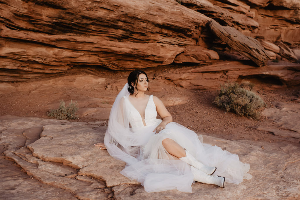 Utah Elopement Photographer captures bride sitting on red rock with white cowboy boots