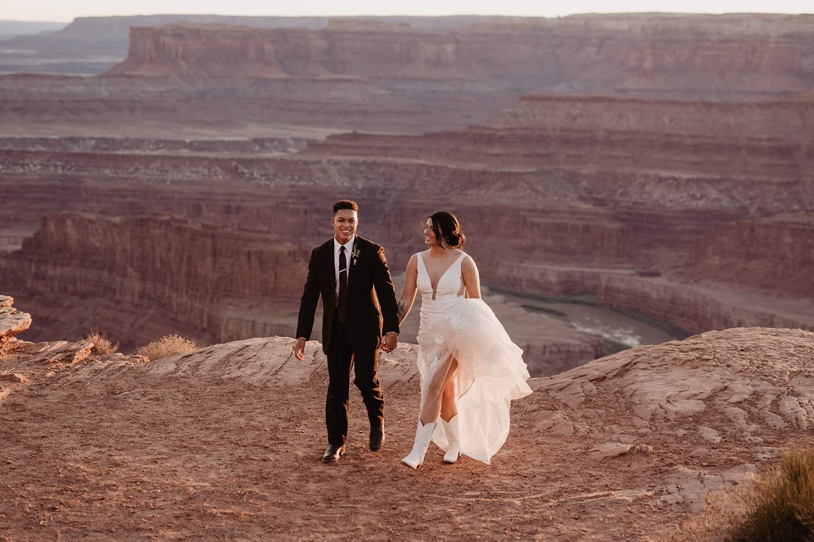 wedding portraits in Arches National Park with bride and groom holding hands and walking on the red rock cliffs together while the sunsets captured by Utah elopement photographer