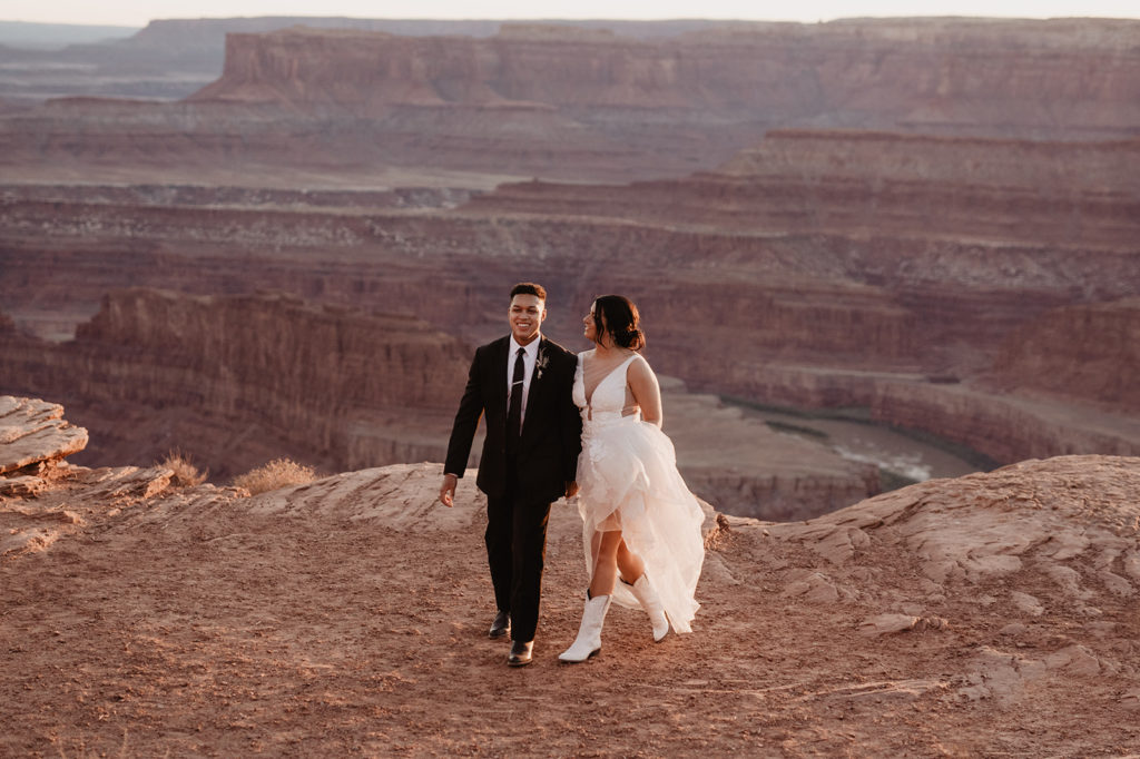 bride and groom walking together at sunset on a mountain top in the desert of moab utah for candid wedding photos by utah elopement photographer