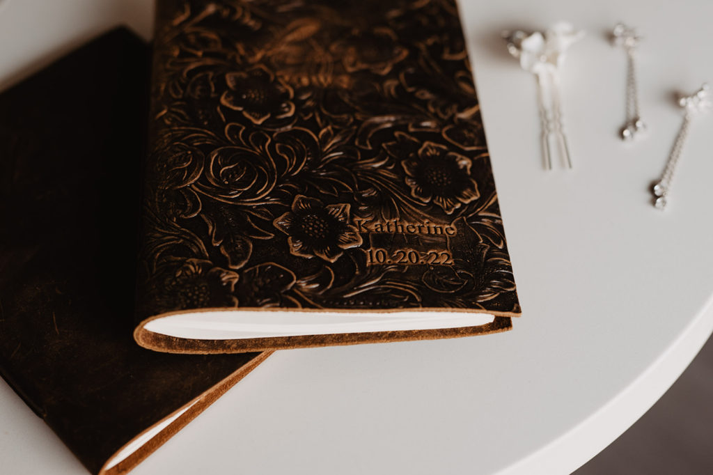 brown leather vow books sitting on a white table next to brides jewelry captured by Utah elopement photographer 