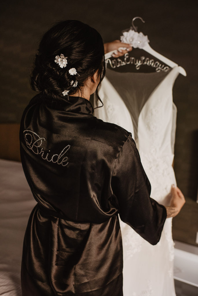 bride in a black robe holding up her lace wedding dress in her bridal suite captured by Utah elopement photographer 