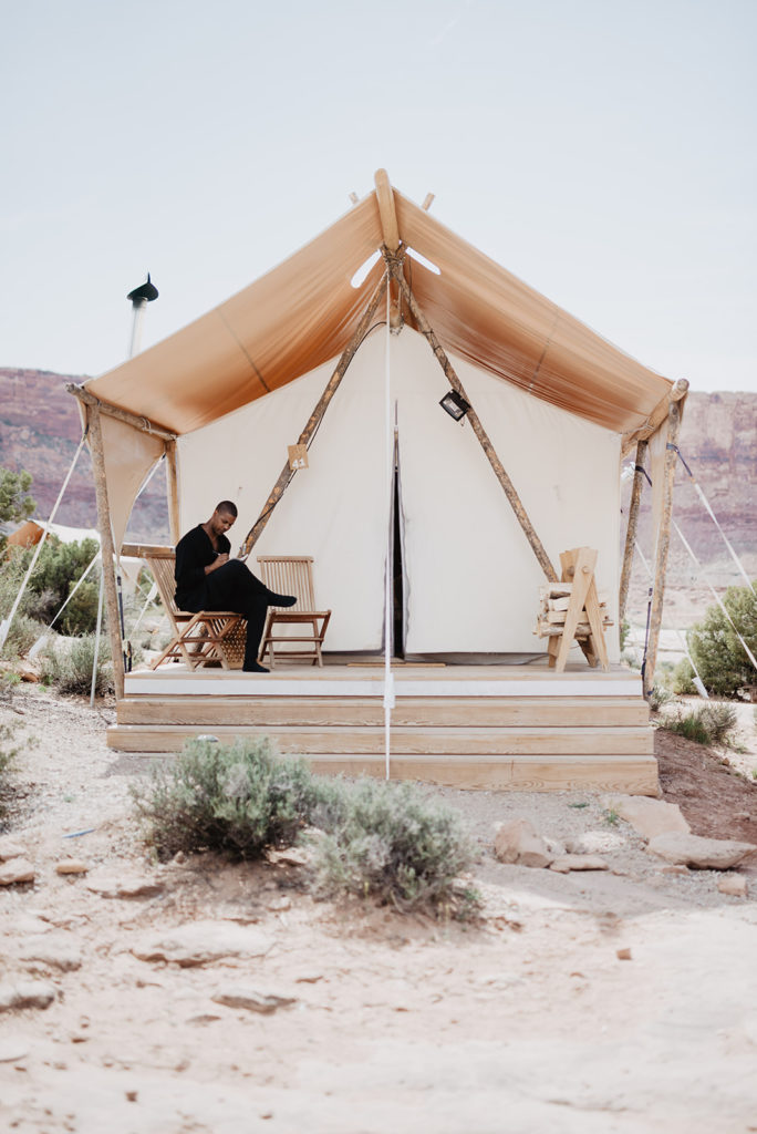 groom sitting outside of his tent in Moab Utah writing his vows for his wedding day 