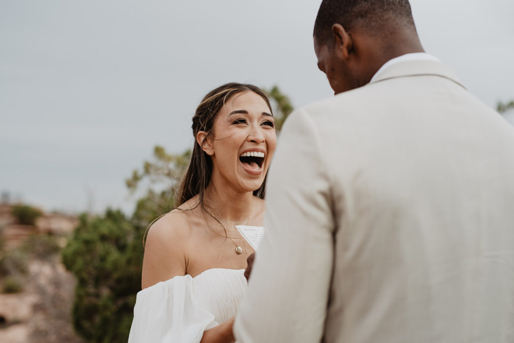 bride excitedly smiles as her groom read vows for their arches national park wedding 