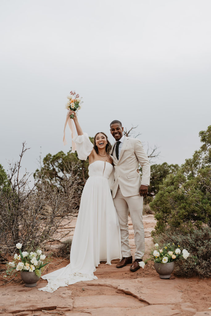 Utah wedding photographer capture bride and groom in Arches National Park celebrating on top of a mountain surrounded by sage brush